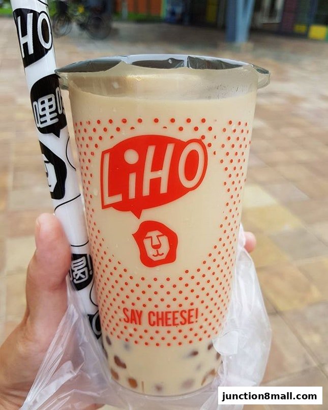 A hand holds a LiHO TEA cup with bubble tea and a branded straw.