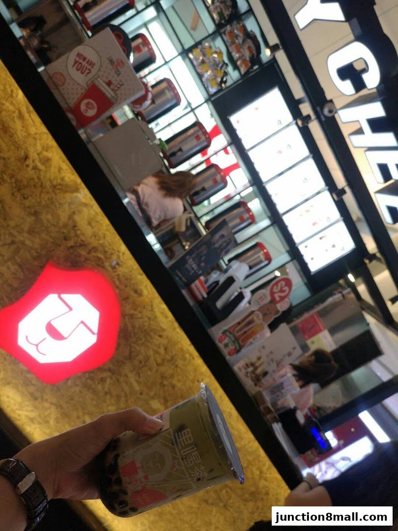 A hand holds a LiHO TEA drink in front of the shop's illuminated logo and menu displays.