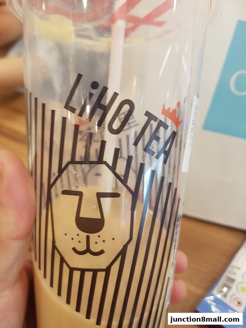 A person holds a LiHO TEA cup with a lion logo and a straw.