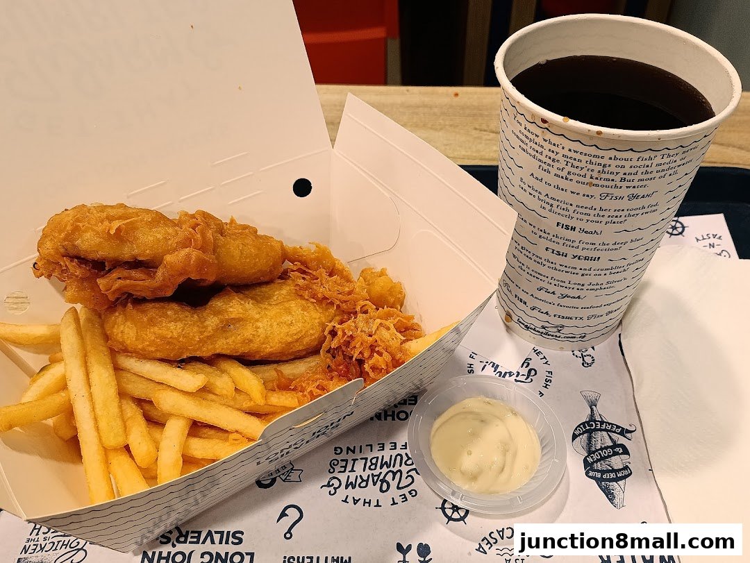 A box of fried fish and chips with a side of tartar sauce and a cup of soda.