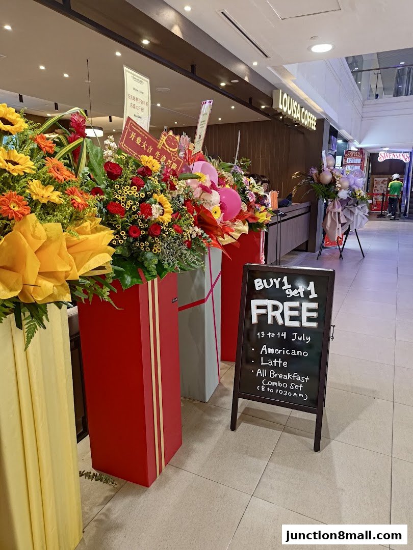 Louisa Coffee shop entrance decorated with celebratory flower arrangements and a promotional sign.