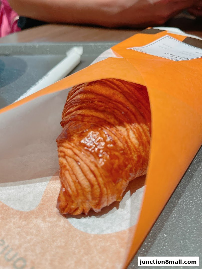 A golden-brown croissant is presented in an orange paper wrapper.