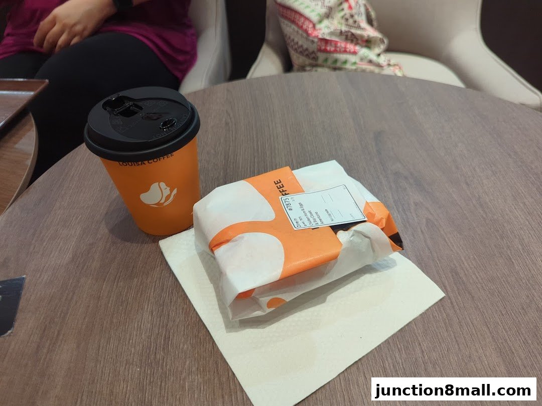 A coffee cup and a wrapped food item on a wooden table at Louisa Coffee.