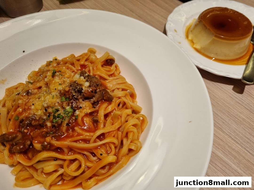A plate of fettuccine pasta with meat sauce and a side of creme caramel dessert.