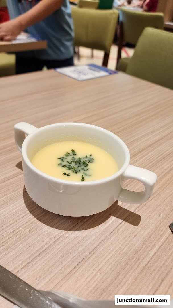 A close-up of a bowl of creamy soup garnished with chopped herbs on a wooden table.