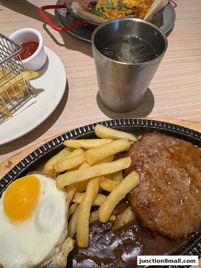 A sizzling steak, fried egg, and french fries served with ketchup and a drink.