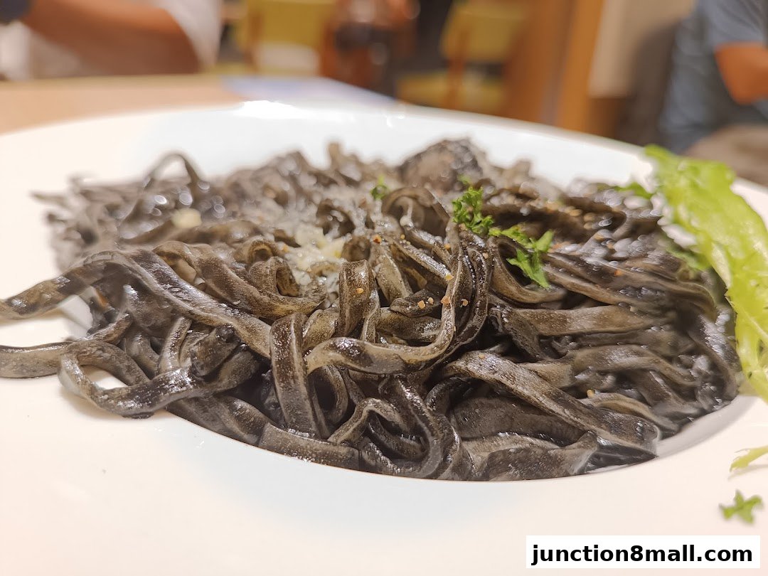 A close-up shot of black squid ink pasta served on a white plate with a garnish.
