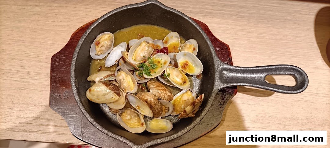 A sizzling dish of clams served in a cast-iron pan with a flavorful broth.