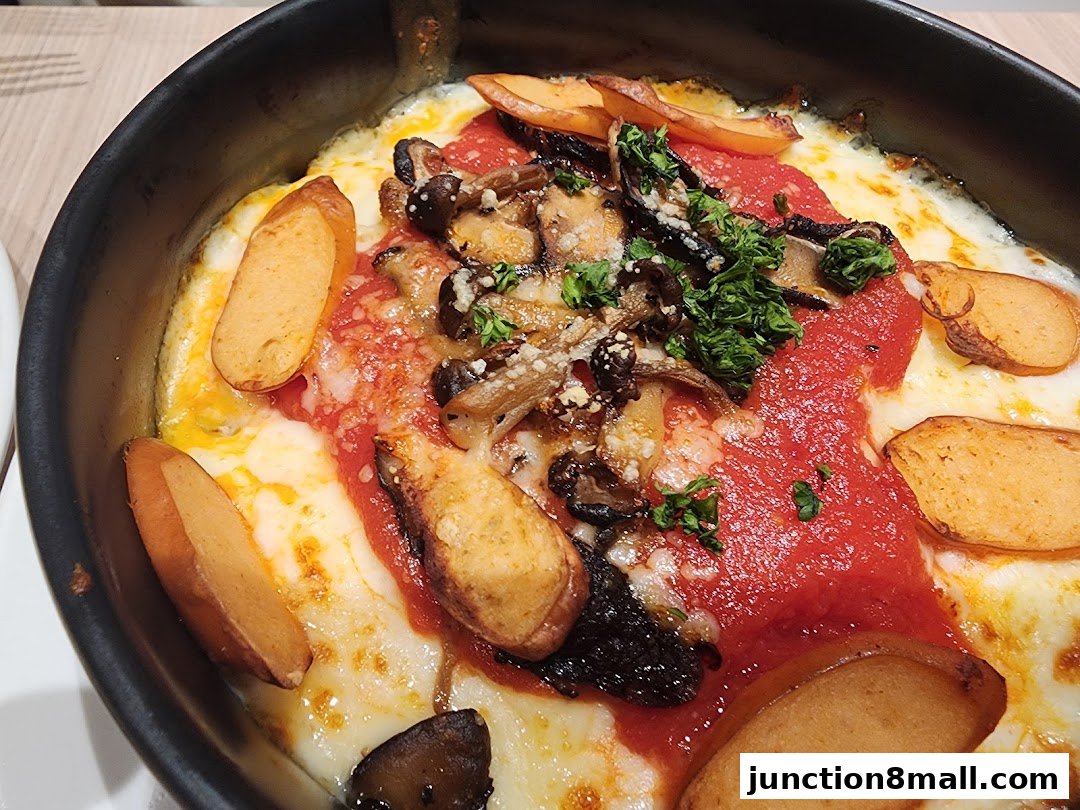 A close-up of a baked dish with cheese, tomato sauce, mushrooms, and sausage slices.