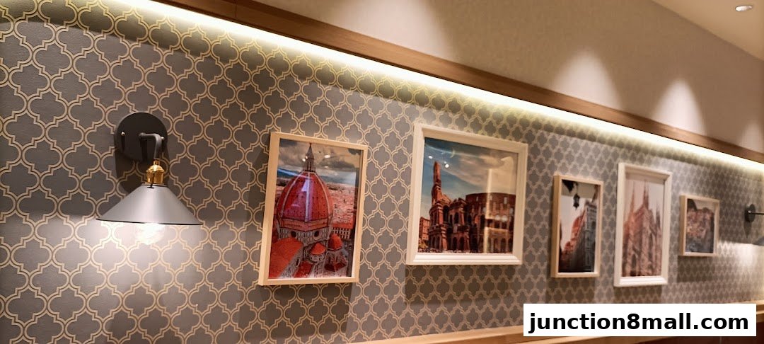A wall with patterned wallpaper, framed pictures of Italian landmarks, and a sconce light.