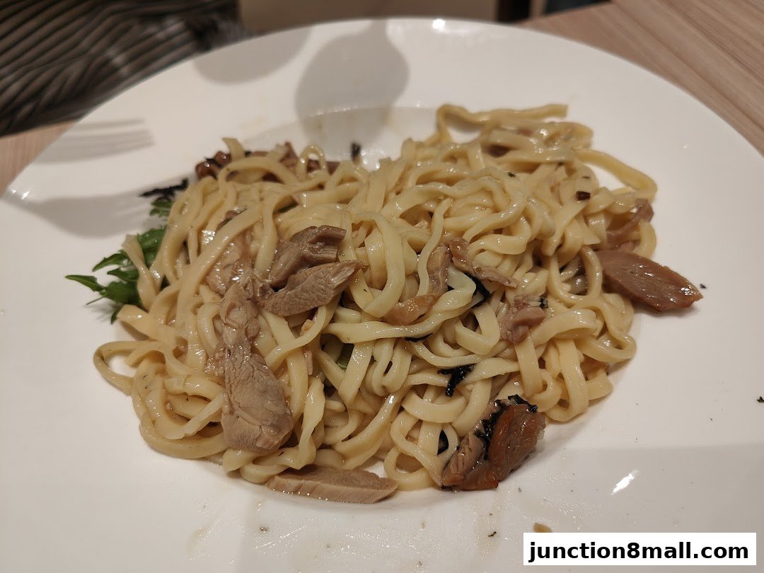 A close-up shot of a plate of noodles with meat and greens.