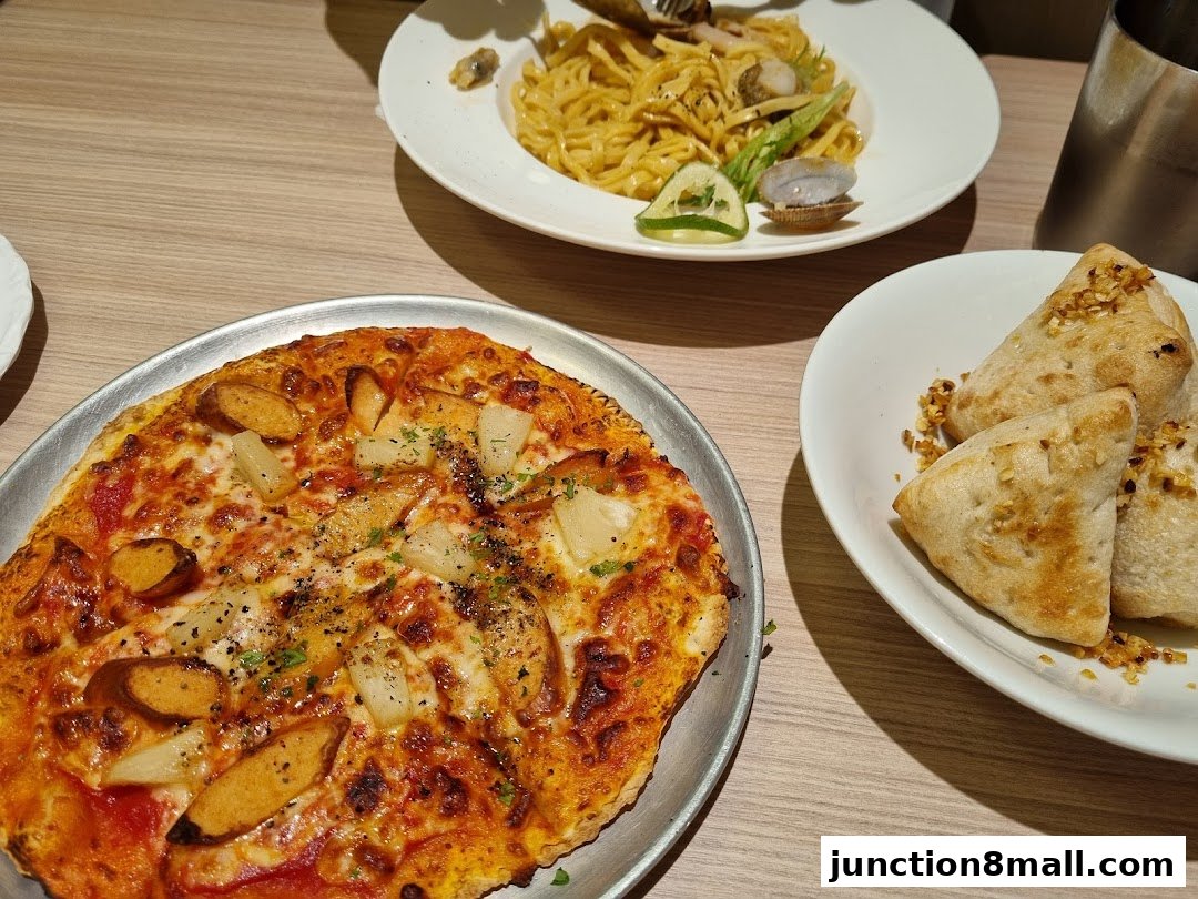 A delicious pizza, pasta, and garlic bread served on a wooden table.