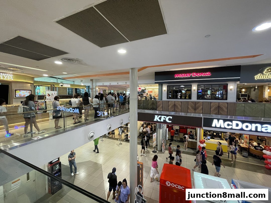 A busy shopping mall interior with various food outlets including Mister Donut, KFC, and McDonald's.