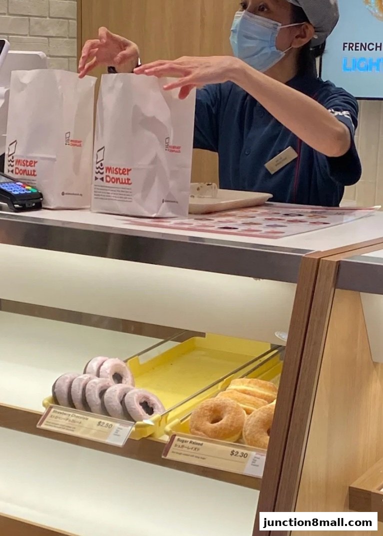 A Mister Donut staff member bags donuts for a customer at the counter.