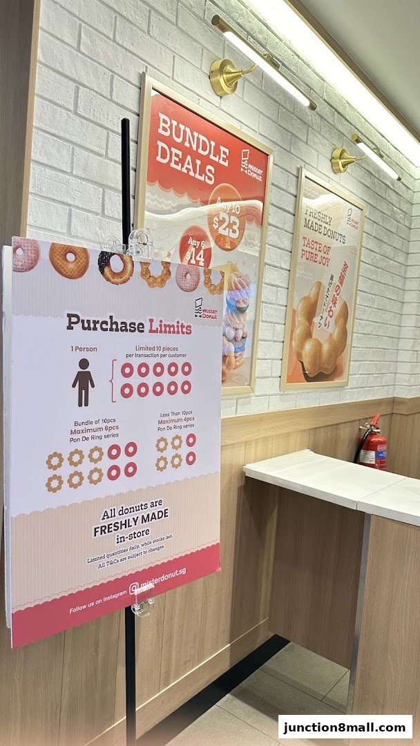 A sign detailing purchase limits and bundle deals for Mister Donut, with promotional posters in the background.