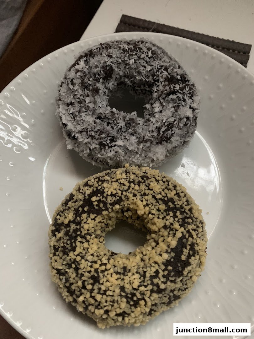 Two delicious donuts, one covered in shredded coconut and the other in chopped nuts, served on a white plate.
