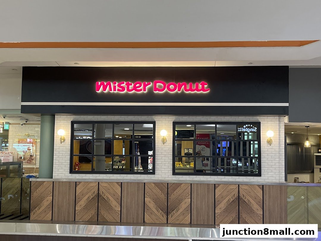 The exterior of a Mister Donut shop with its illuminated logo and modern wooden facade.