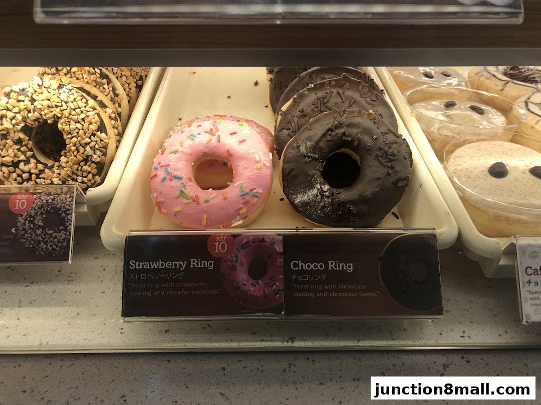 A display case filled with various donuts, including strawberry and chocolate ring varieties.