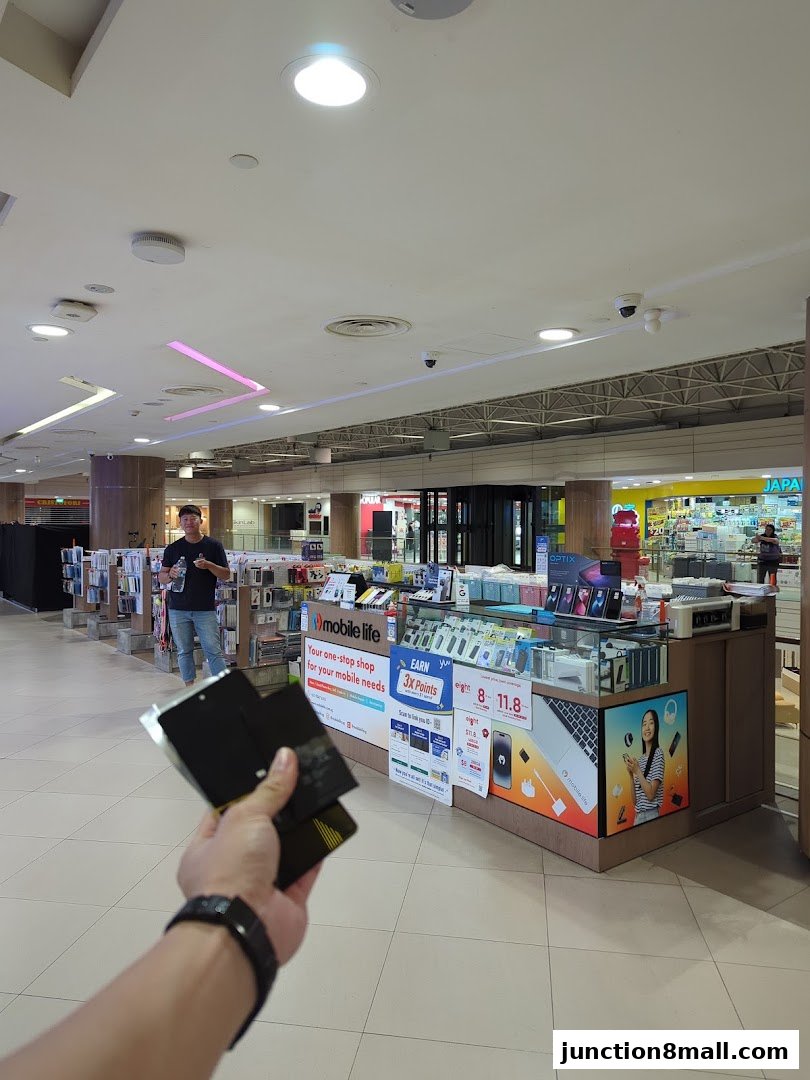 A person holds phone accessories in front of a Mobile Life shop in a mall.