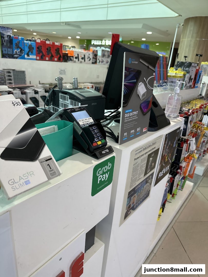 A retail counter with a payment terminal, phone accessories, and promotional materials.