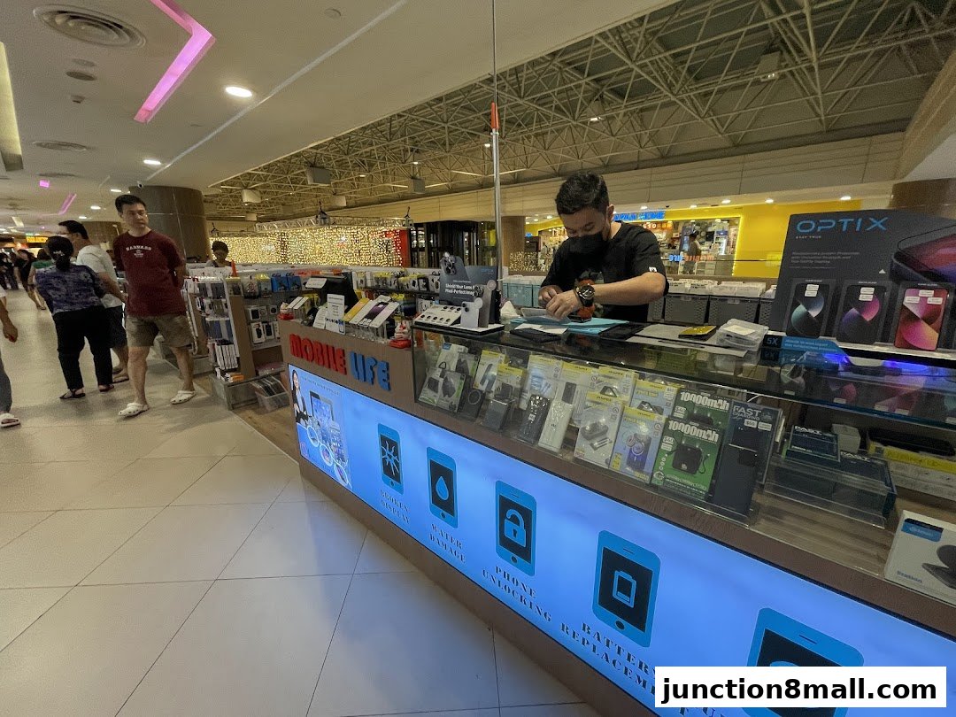 A mobile phone repair shop counter with a technician working and various phone accessories displayed.