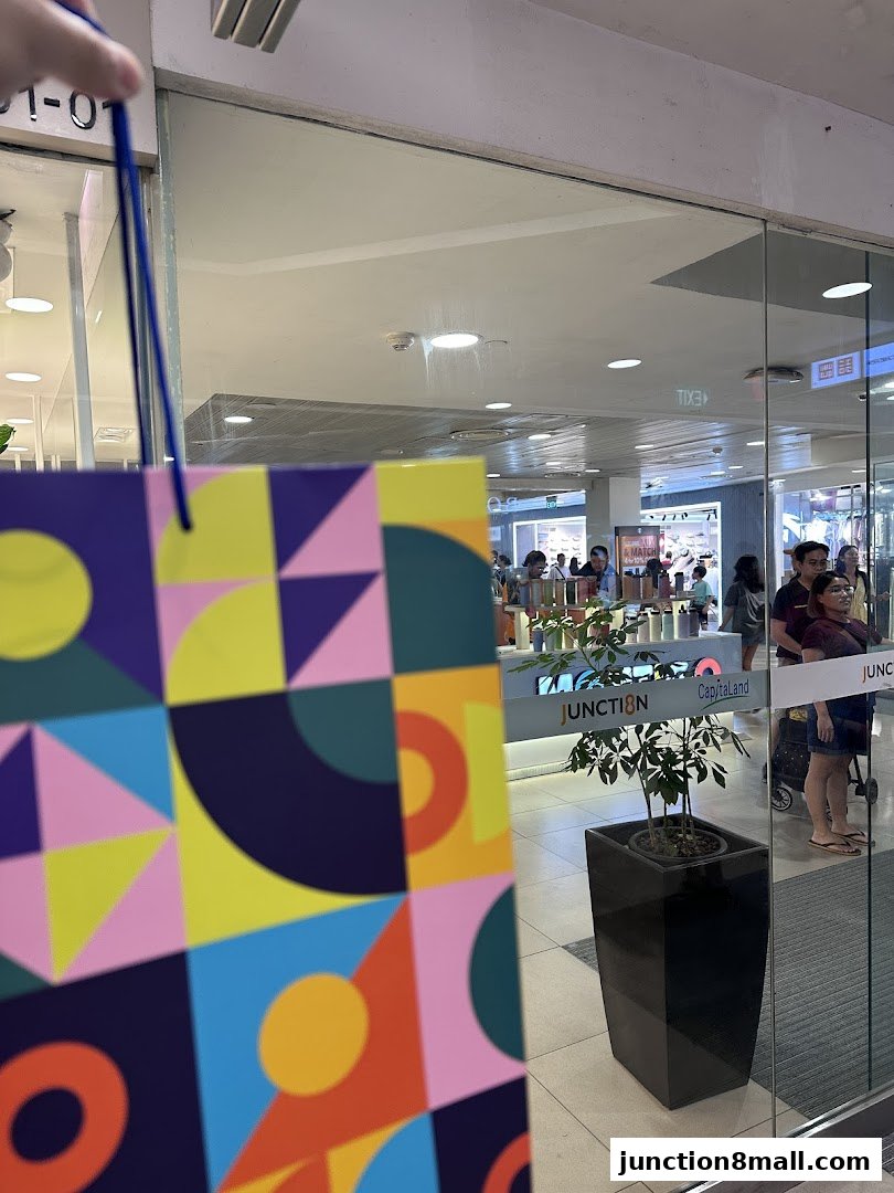 A colorful shopping bag is held in front of a store entrance with people inside.