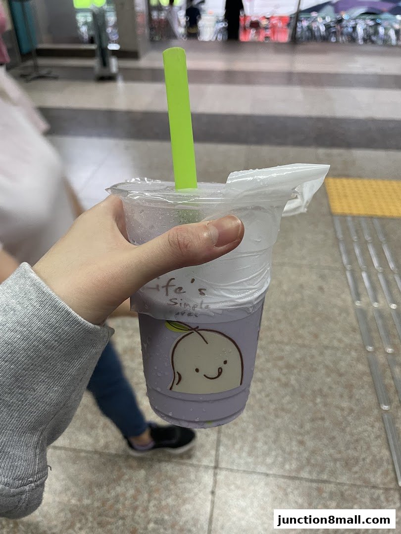 A hand holds a purple drink with a green straw and a cute peach illustration.