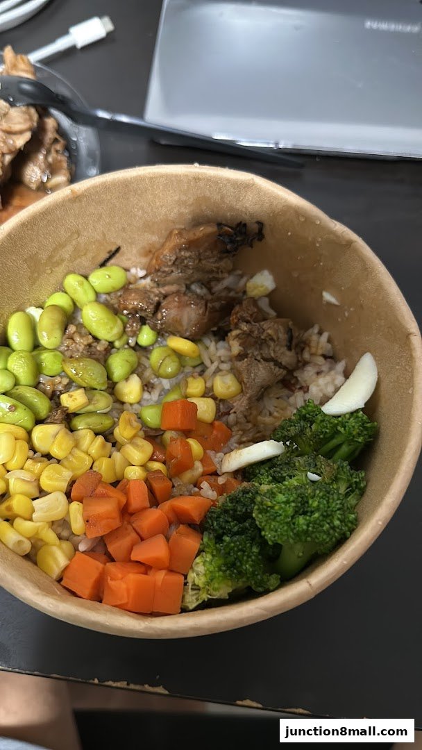 A bowl of rice topped with chicken, edamame, corn, carrots, and broccoli.