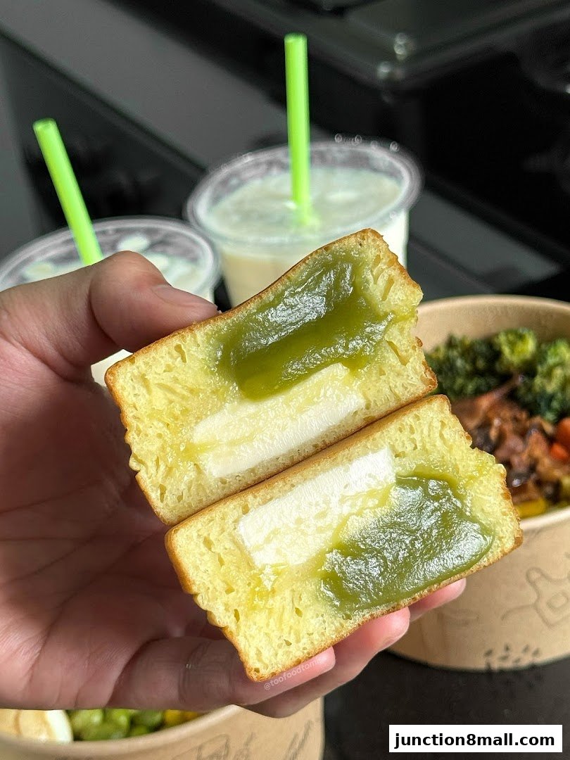 A person holds a cut-open sweet pastry filled with green paste and cream, with drinks in the background.