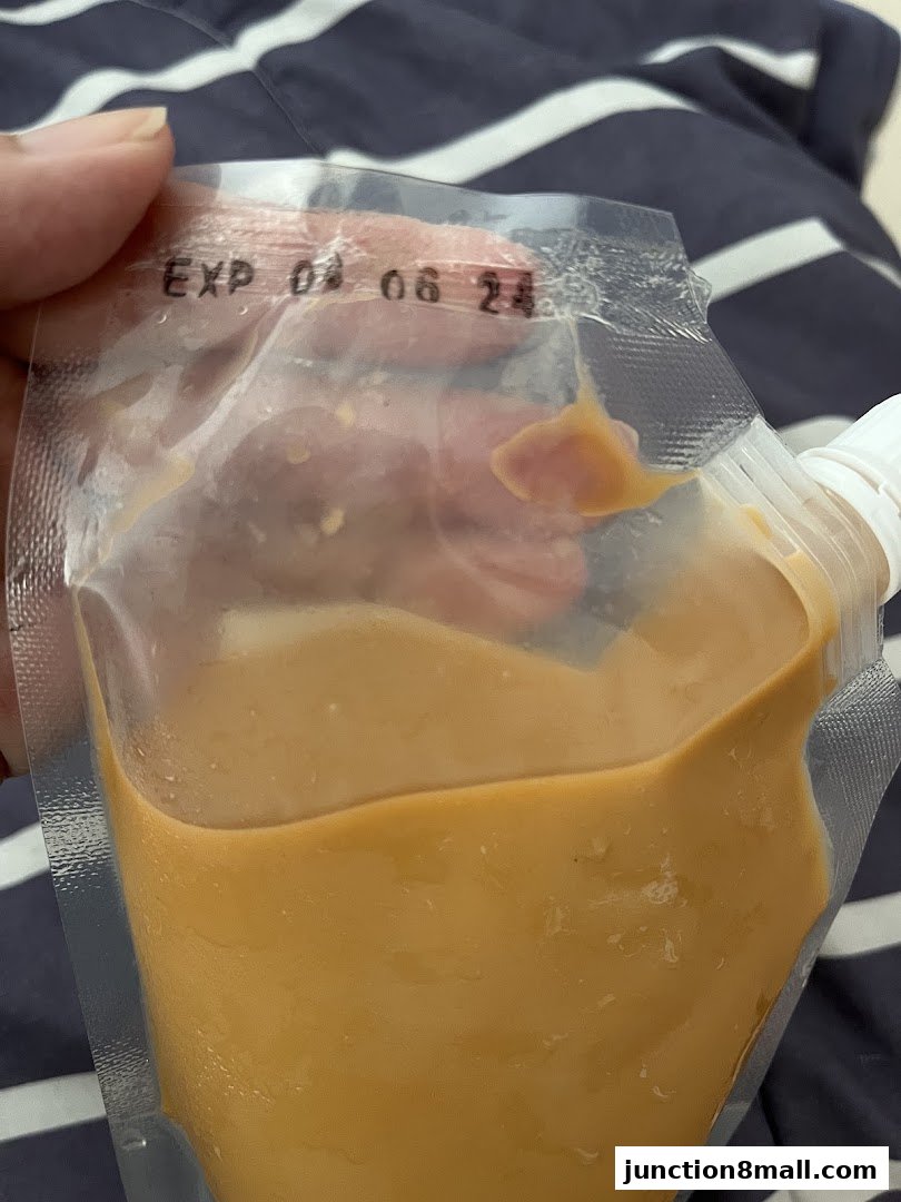 A hand holds a pouch of creamy orange sauce with an expiration date visible.