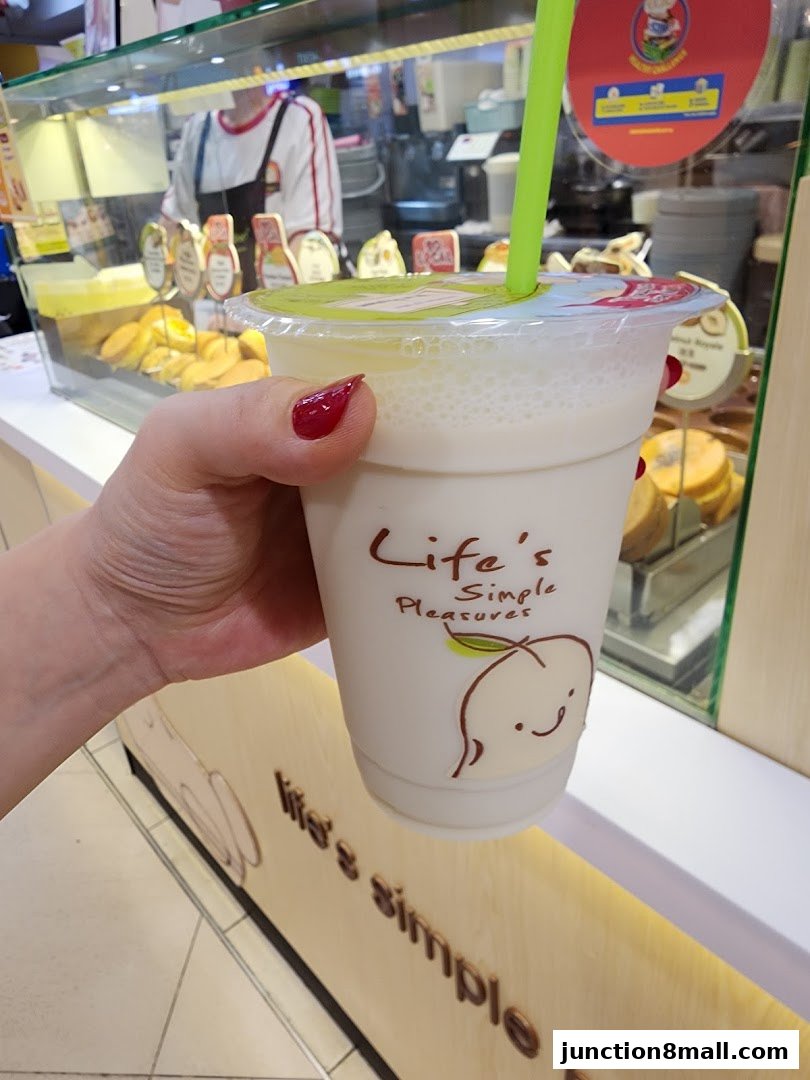 A hand holds a creamy beverage with a green straw in front of a shop display.