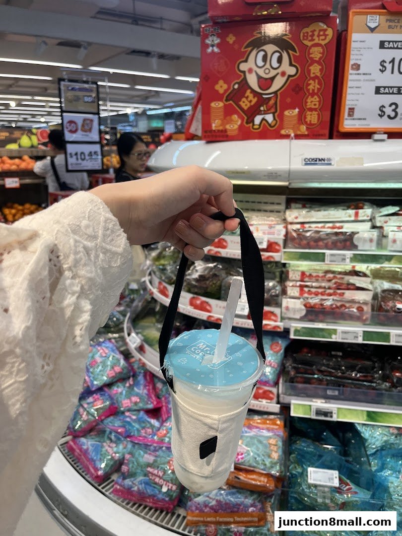A hand holds a Mr. Coconut drink in a reusable sleeve in front of grocery store shelves.