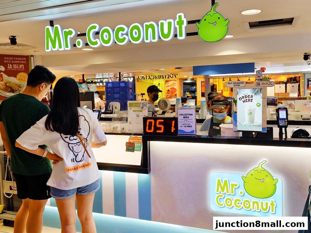 A couple stands at the counter of Mr. Coconut, a beverage shop with bright signage.