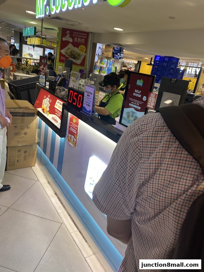 A Mr. Coconut Junction 8 shop counter with staff serving customers and a self-order kiosk.