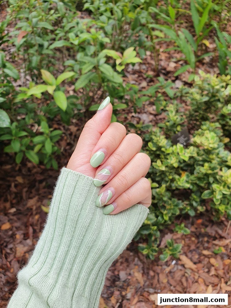 A hand with light green nails featuring abstract white lines, wearing a light green sweater.