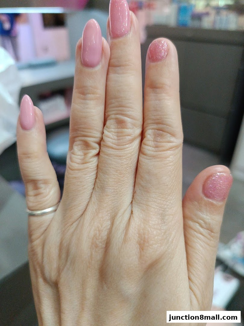 A close-up of a hand with perfectly manicured pink nails, showcasing a glossy finish and subtle glitter.