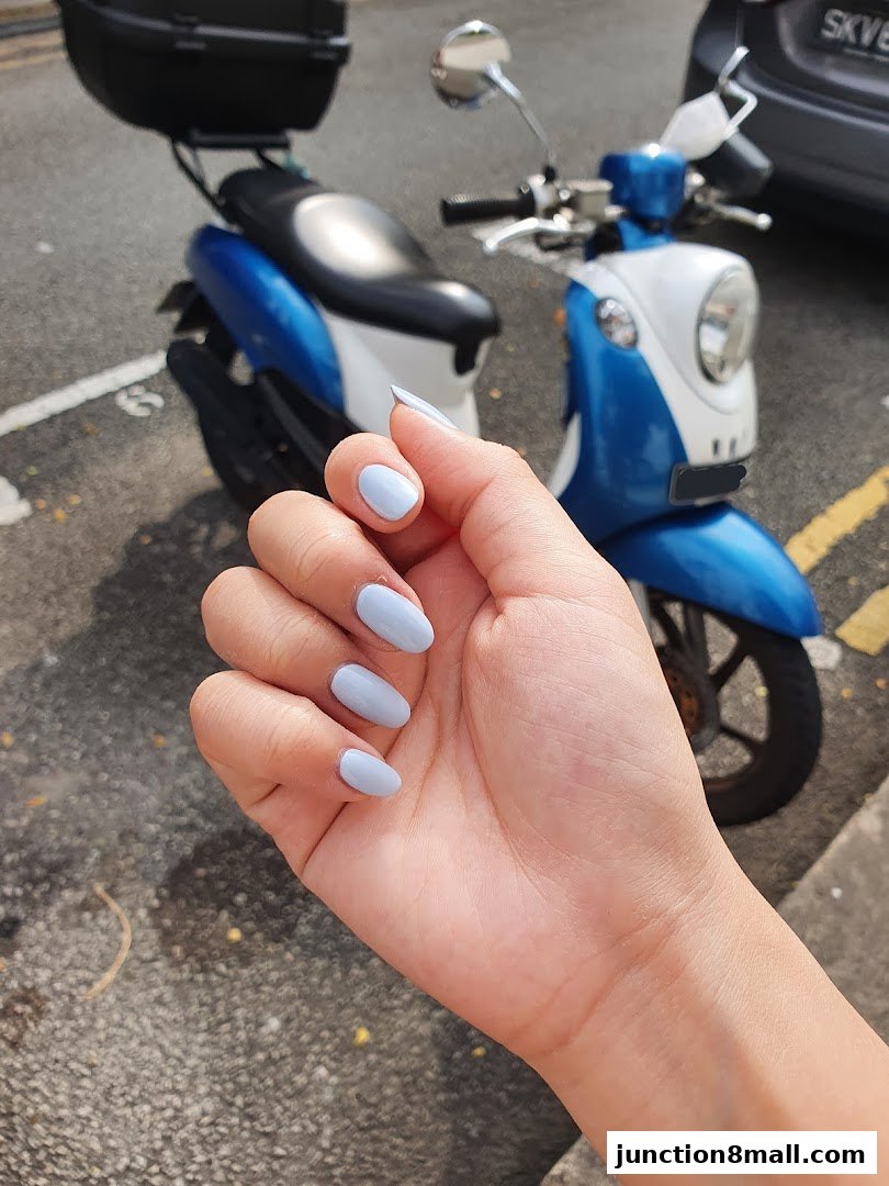 A hand with light blue nails is shown in front of a blue and white scooter.