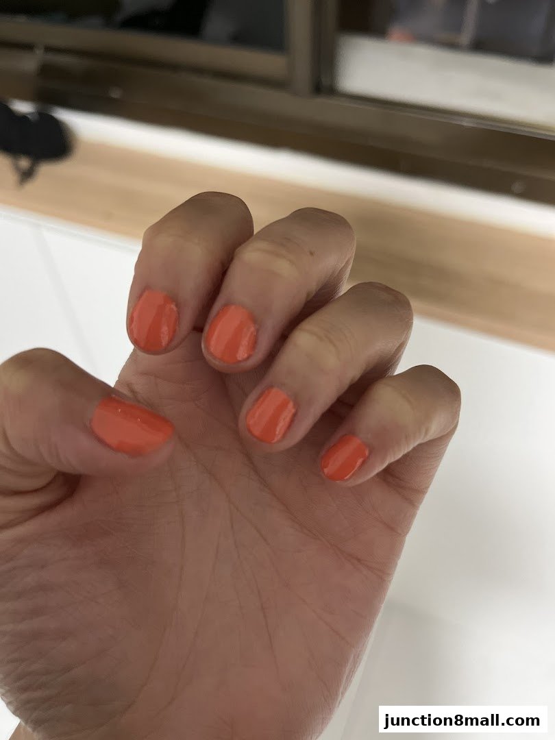 A close-up shot of a hand with perfectly manicured nails painted in a vibrant coral shade.