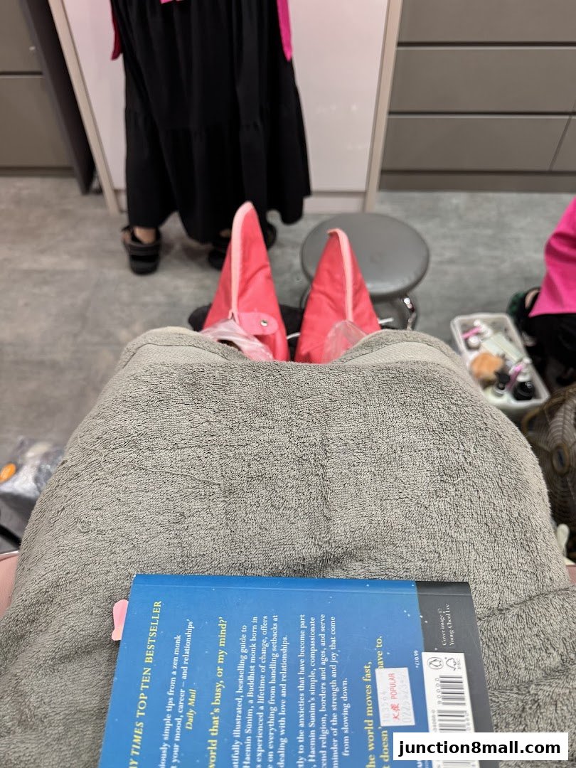 A person's feet are covered in pink booties while reading a book during a nail salon visit.