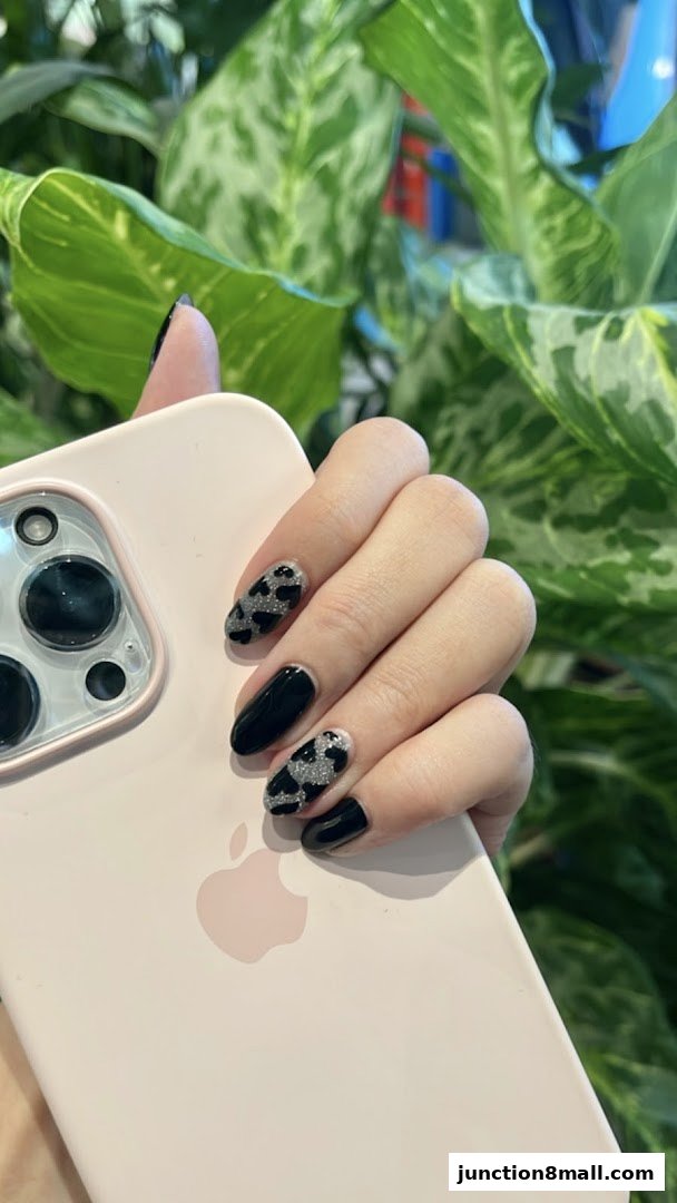 A hand with stylish black and glittery nails rests on a pink phone case.