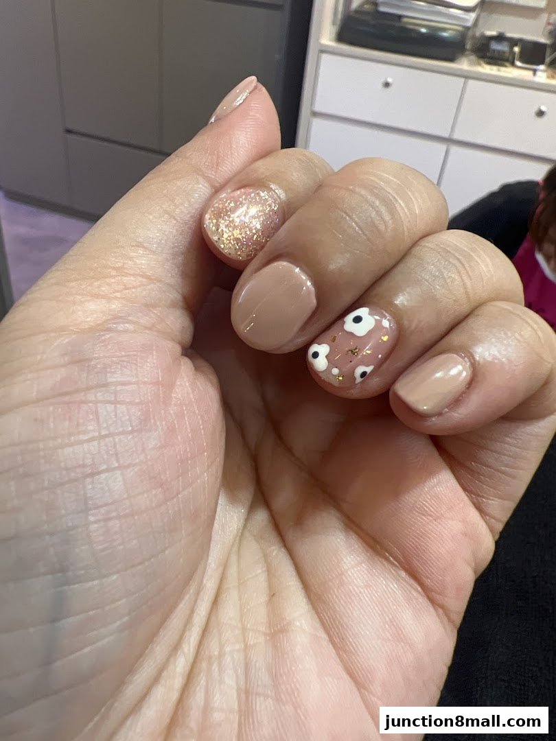 A close-up of a hand showcasing beautifully manicured nails with a nude polish and glitter accent.