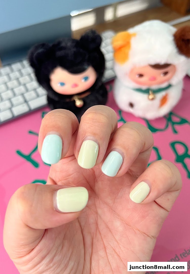 A hand with pastel blue and yellow nails, with cute plush toys in the background.
