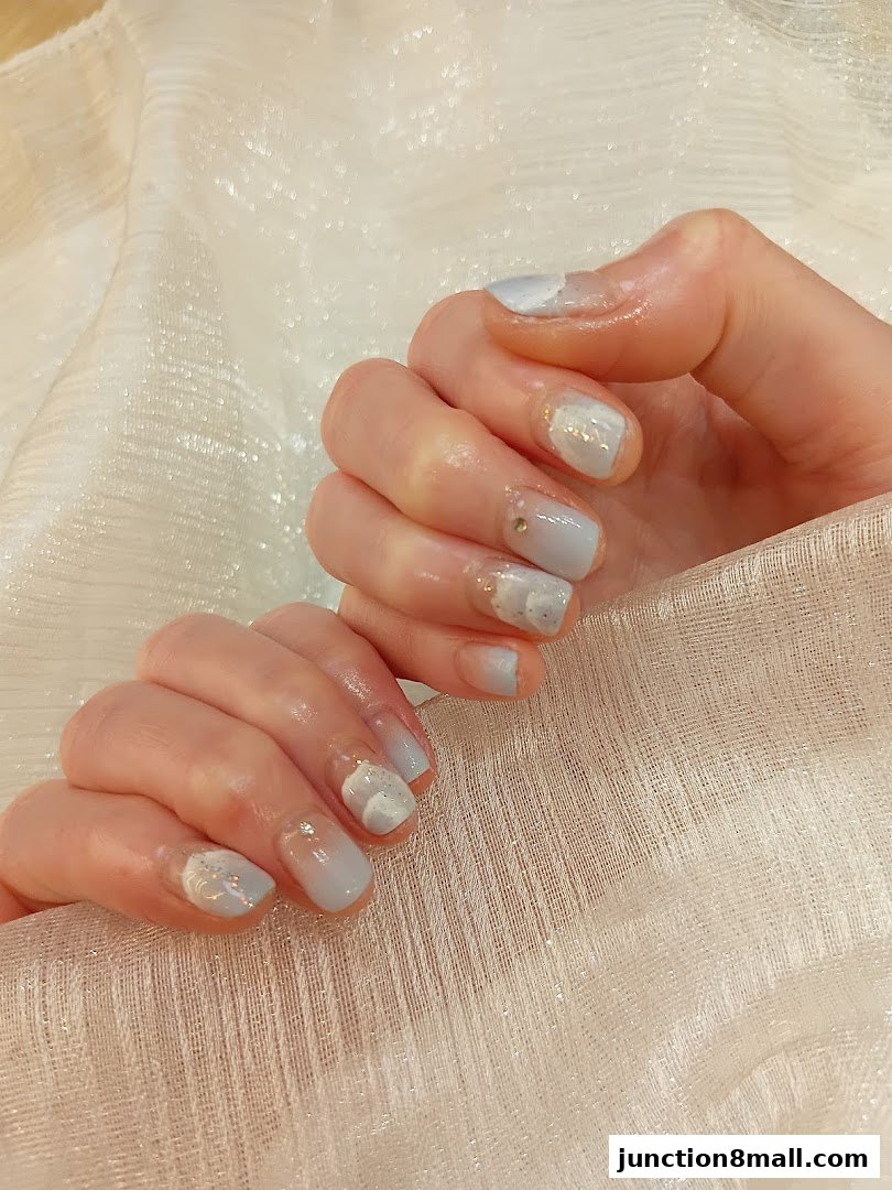Close-up of hands with elegant light blue and white gradient nail art with glitter accents.