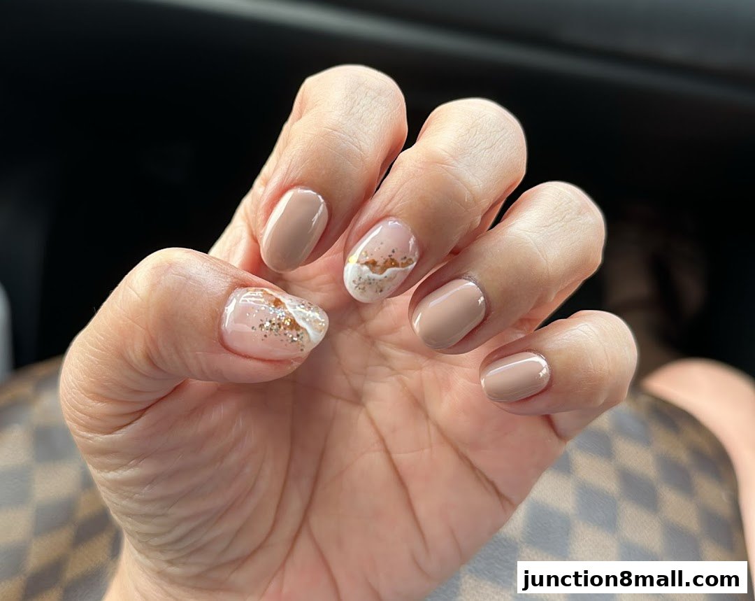 A close-up of a hand with beautifully manicured nails featuring a nude polish and glitter accents.