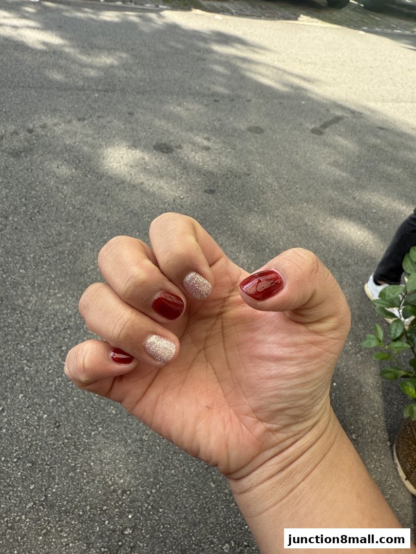 A close-up of a hand with a fresh manicure featuring dark red and glitter polish.