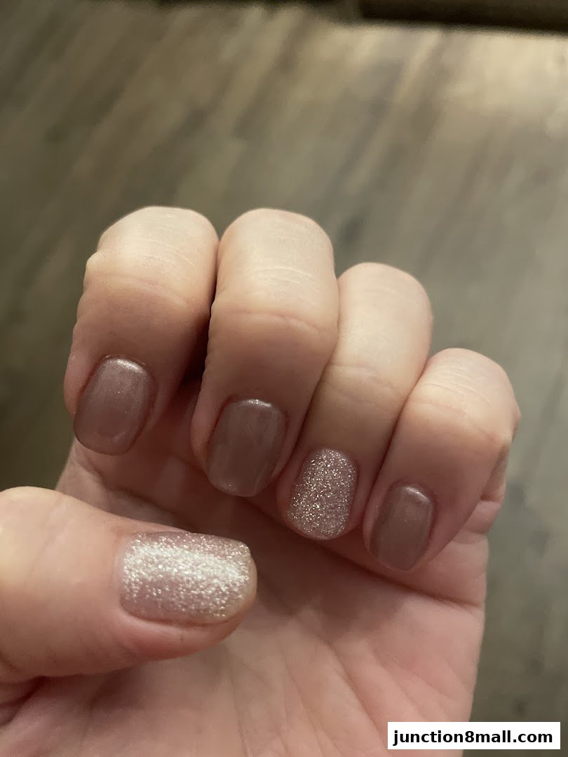 Close-up of a hand with a stylish manicure featuring nude and glitter polish.
