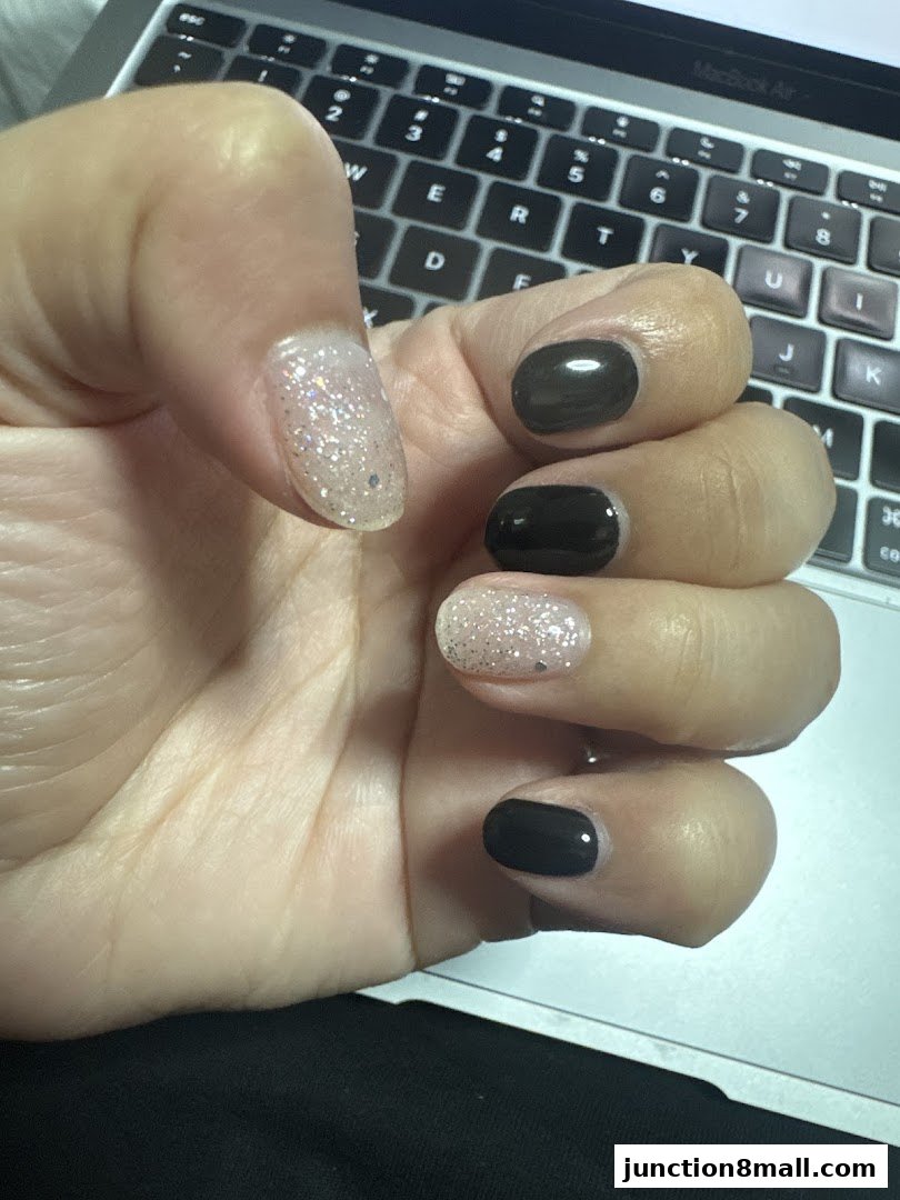 A hand with black and glittery nails rests on a laptop keyboard.
