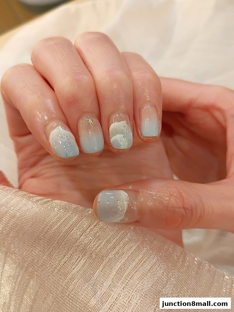 Close-up of a hand with light blue and white gradient nails adorned with glitter.