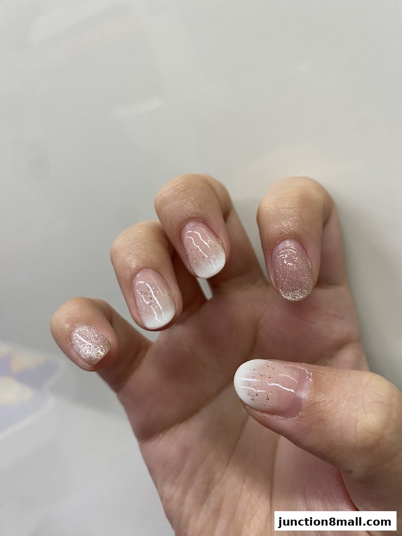 A close-up of a hand with beautifully manicured nails featuring a French tip and glitter accents.