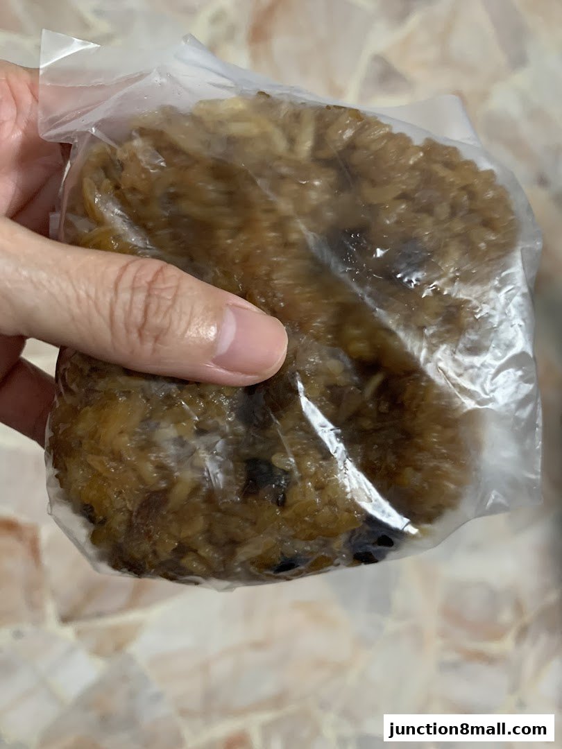 A hand holds a plastic-wrapped savory rice dumpling with visible ingredients.